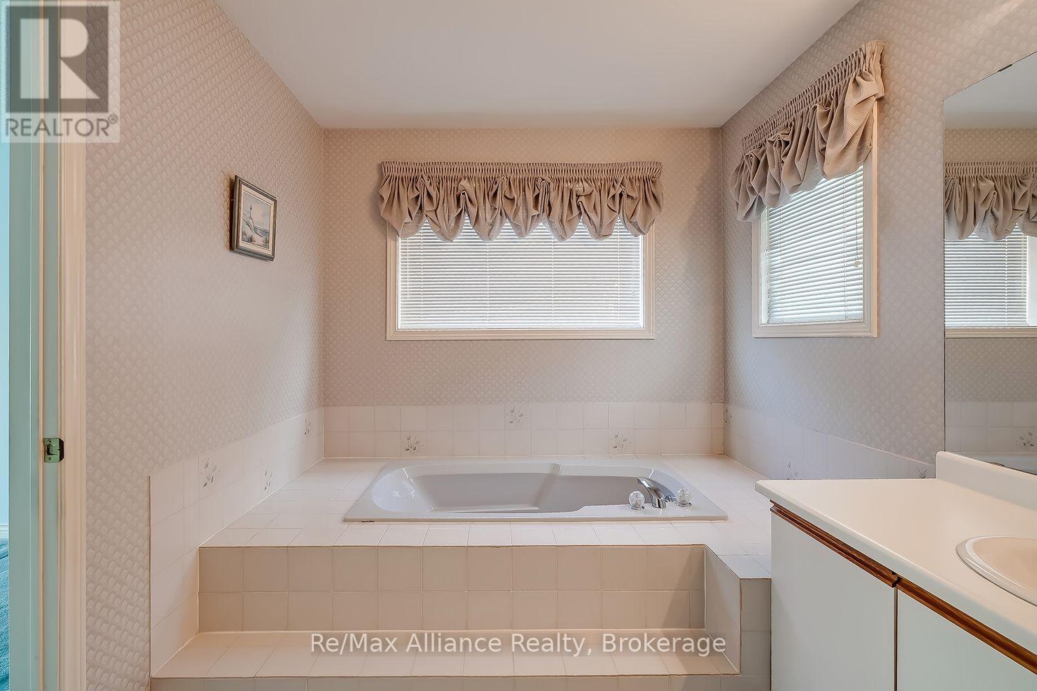 Bathroom with a raised built-in soaking tub, tiled surround, two windows, and a mirrored vanity.