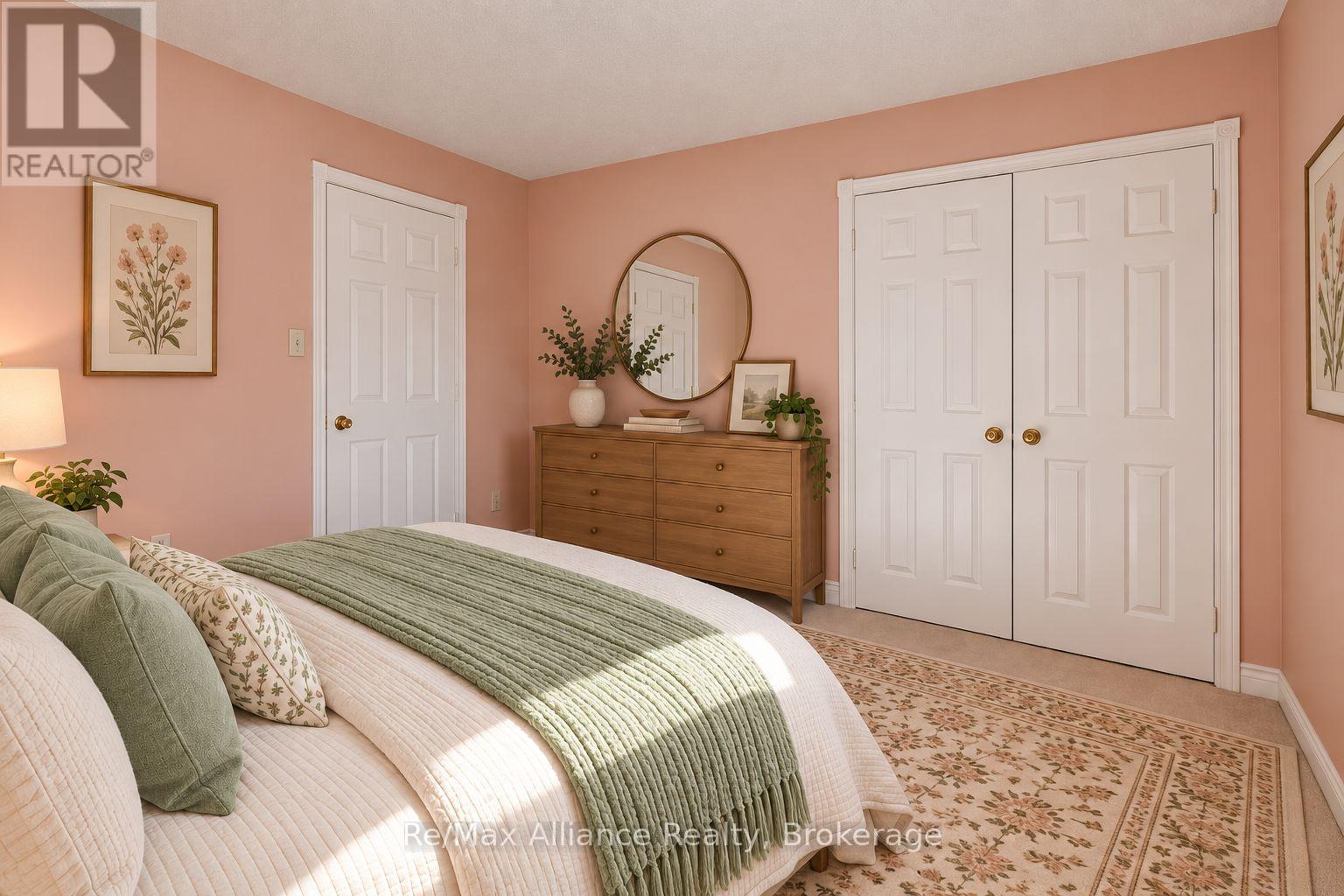 Staged bedroom with sage-green bedding, a wooden dresser, white closet doors, and a floral rug.