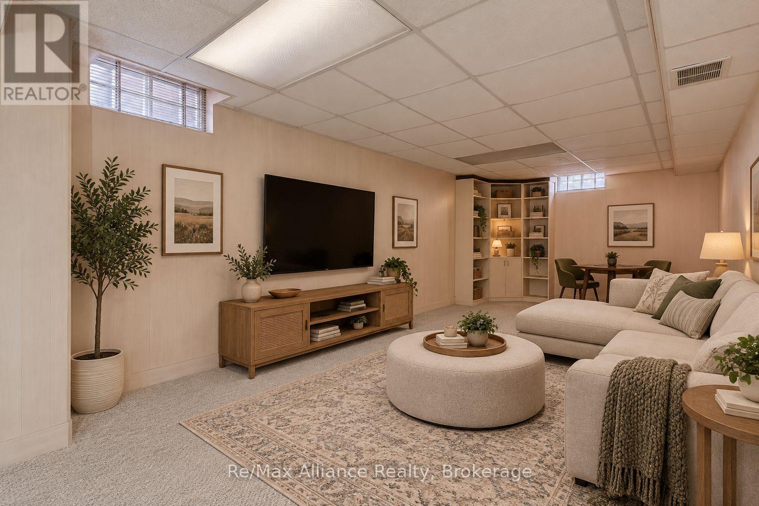 Furnished living room with a large sectional, round ottoman, wall-mounted television, and built-in shelving.