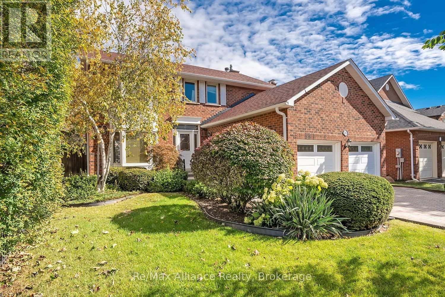 Two-storey red-brick house with a double garage and landscaped front yard beneath autumn trees.