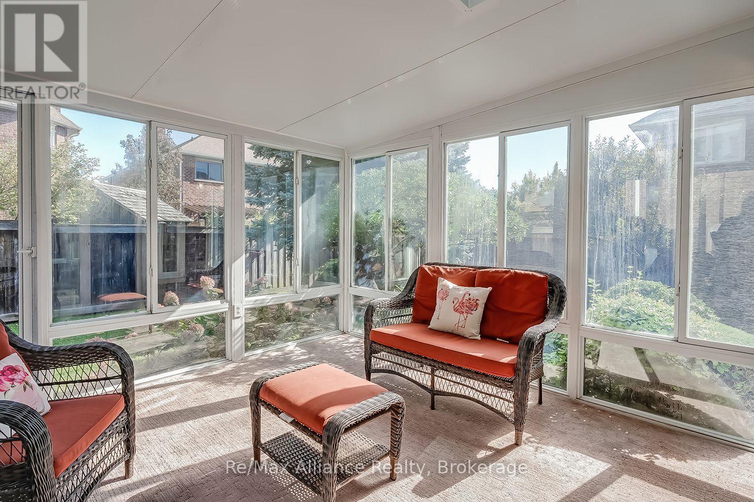 Sunroom with wicker seating, coral cushions, and large windows overlooking a fenced garden.