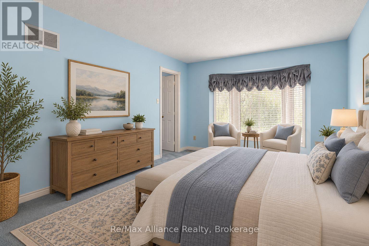 Bedroom with pale blue walls, a cream-and-gray bed, wooden dresser, and armchairs by a bright window.