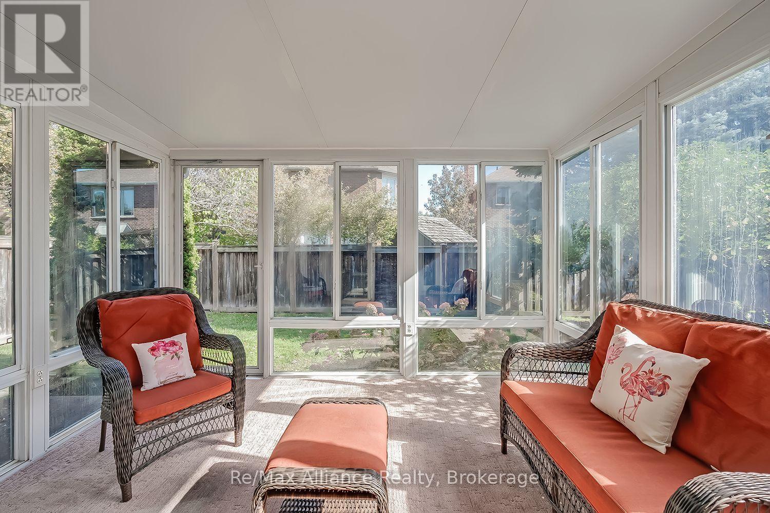 Furnished sunroom with wicker seating and coral cushions, surrounded by windows overlooking a fenced backyard.