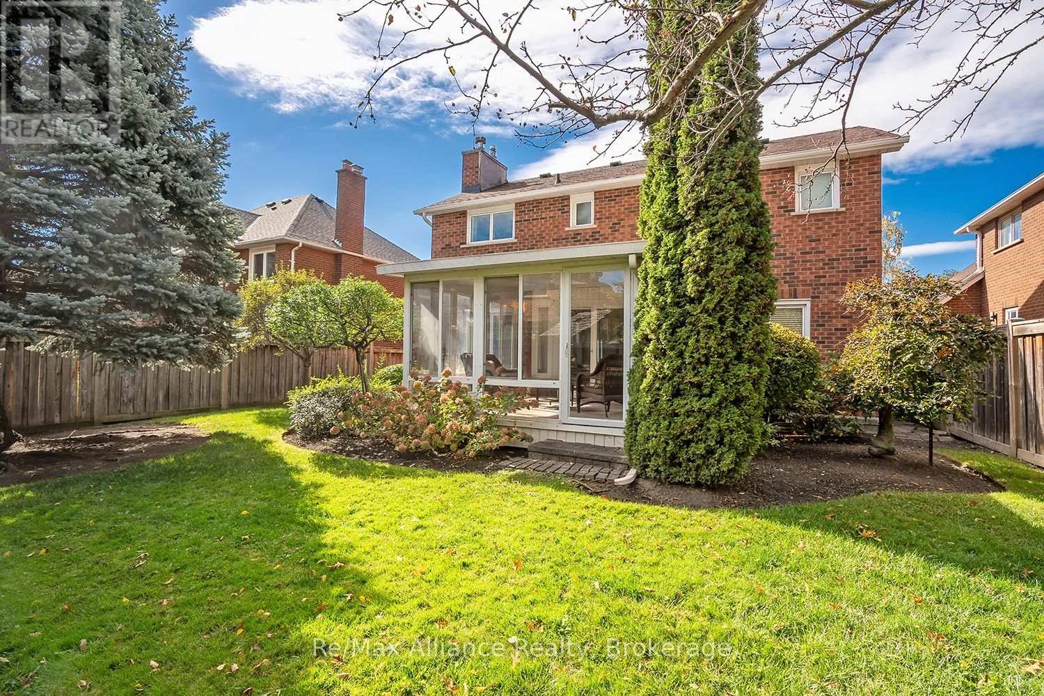 Two-story brick home and glass-enclosed sunroom viewed from its landscaped backyard.