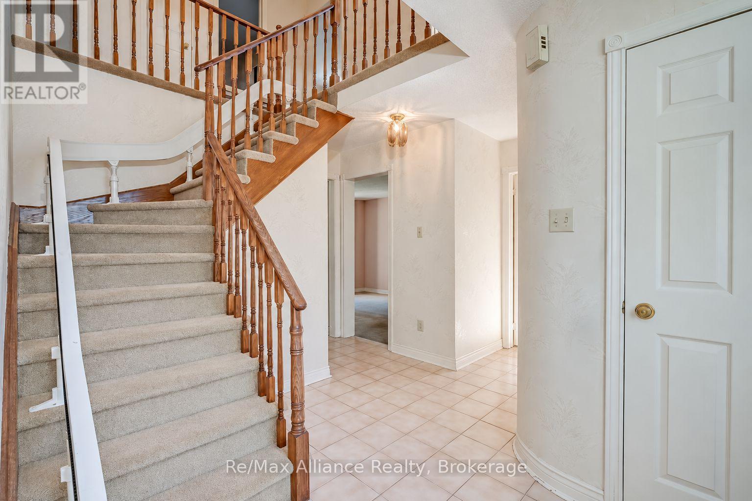 Foyer with a carpeted staircase, ornate wooden railings, tiled floor and white front door.