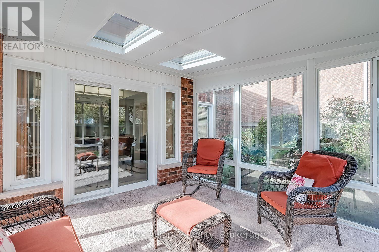 Enclosed sunroom with skylights, large windows, and wicker chairs with coral cushions.