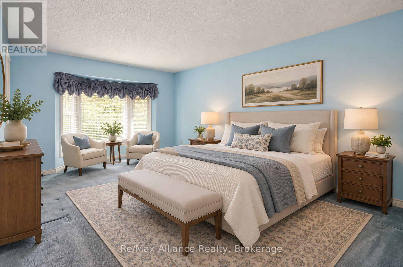Furnished bedroom with a large upholstered bed, blue walls, and armchairs beside a bright window.