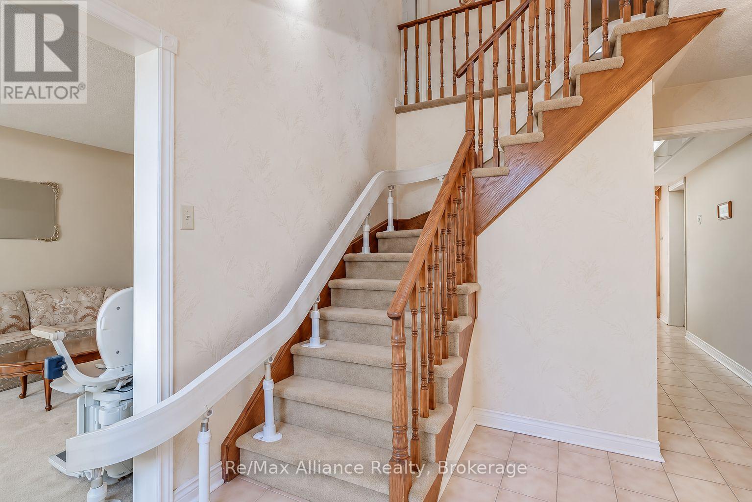 Carpeted staircase with wood railings, an upper landing, and a stair lift.