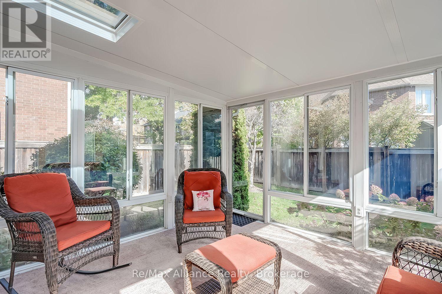 Sunroom with wicker seating, coral-red cushions, floor-to-ceiling windows, and a skylight.