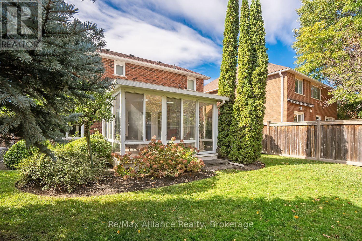 Rear of a red-brick home with a glass-enclosed sunroom and landscaped fenced yard.