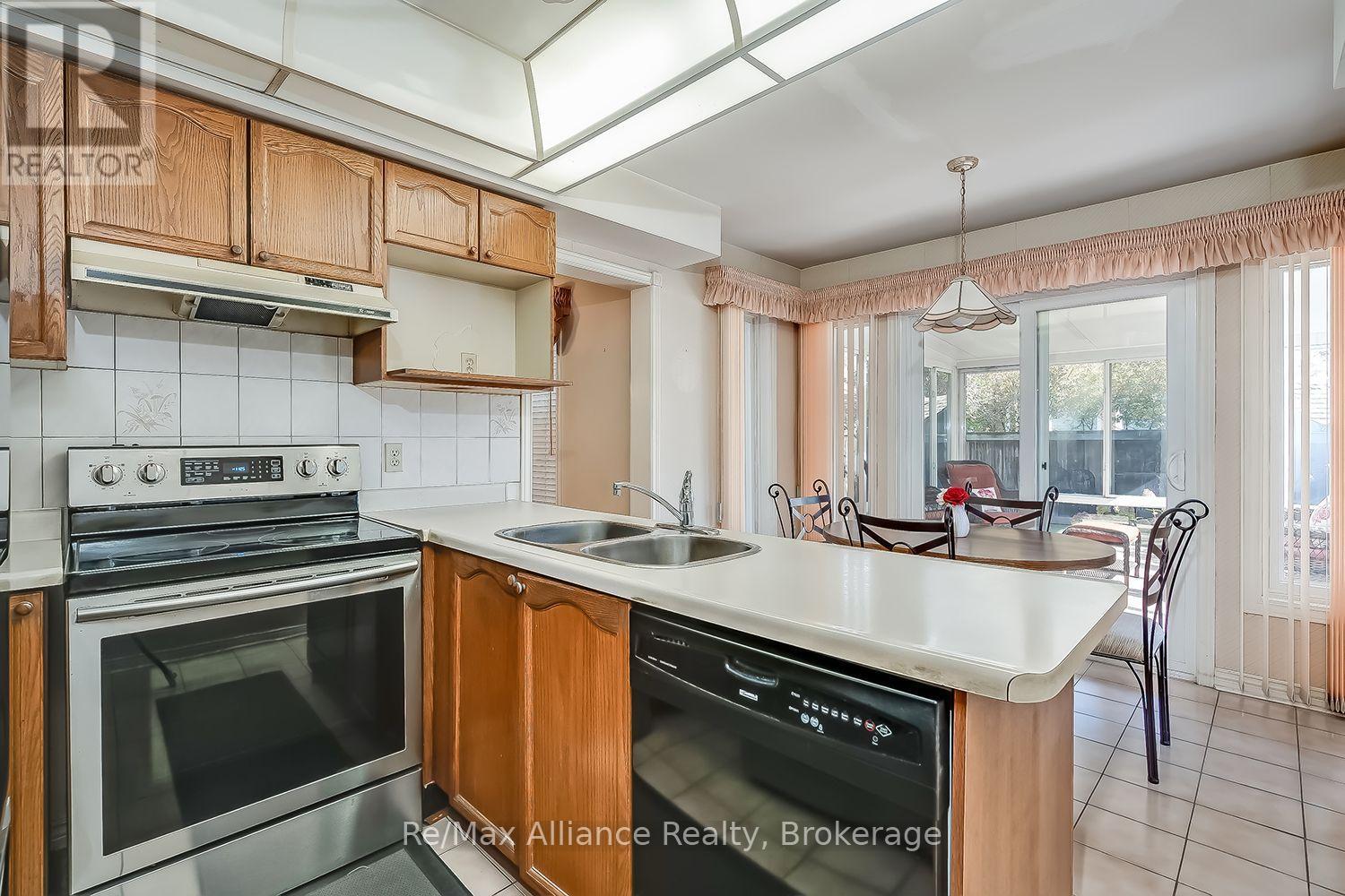 Kitchen with oak cabinets, a white double-sink peninsula, and an adjoining dining area by large windows.