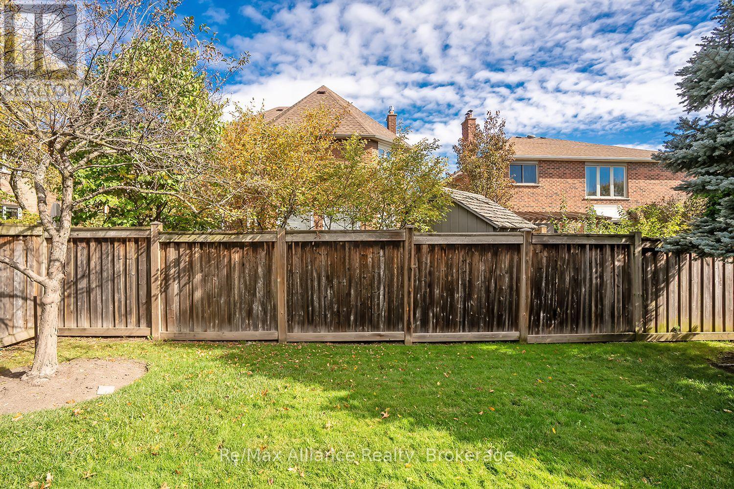 Backyard with a tall wooden privacy fence, green lawn, mature trees, and neighboring brick homes.