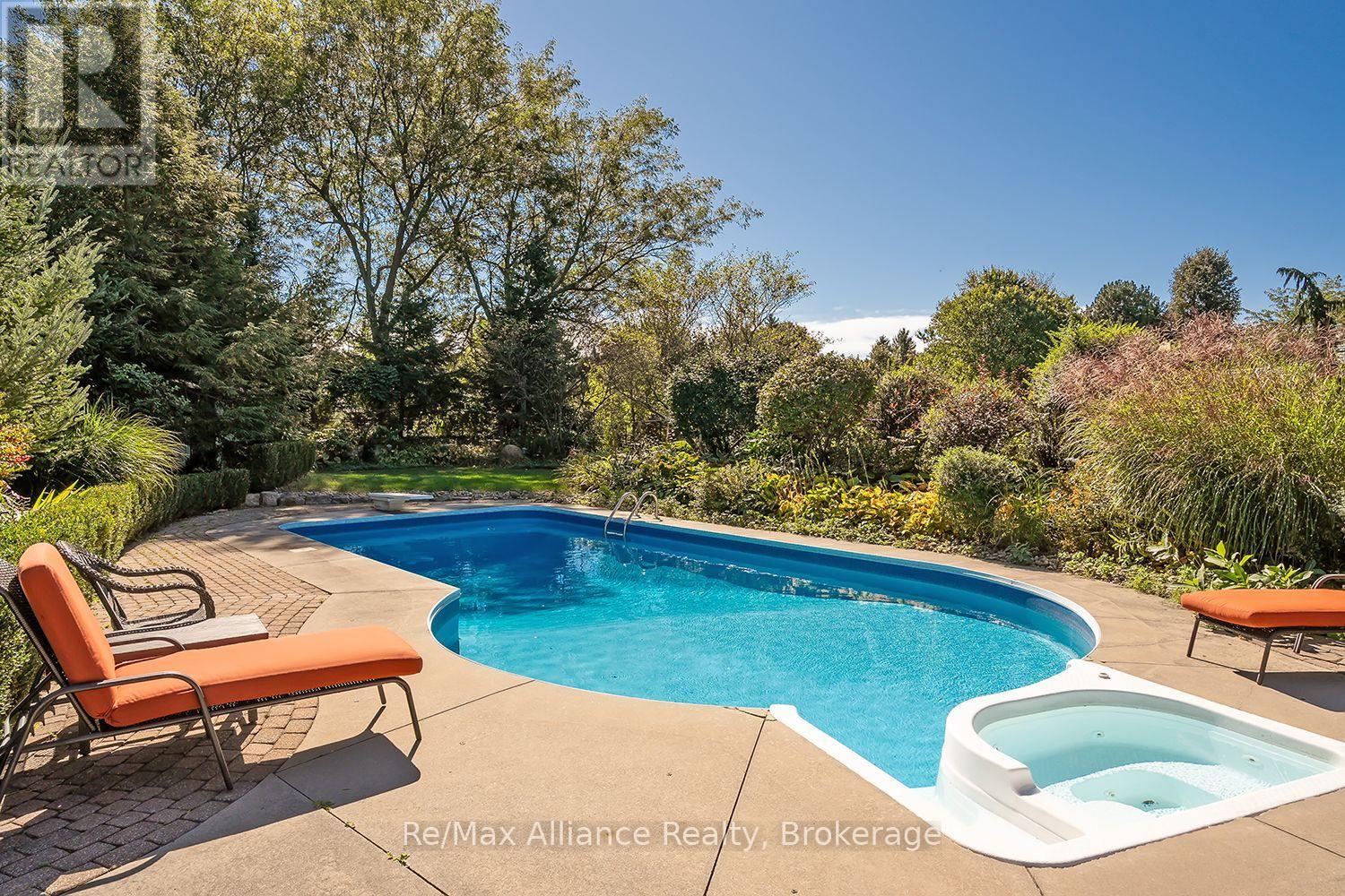 Backyard swimming pool and hot tub surrounded by mature trees and patio seating.