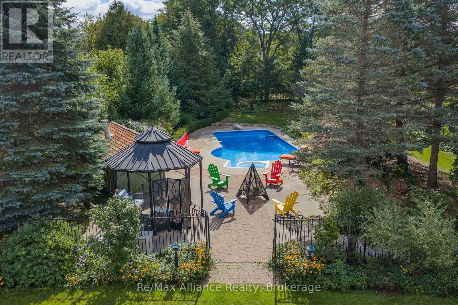 Backyard pool and patio surrounded by mature trees, with a gazebo and colorful Adirondack chairs.