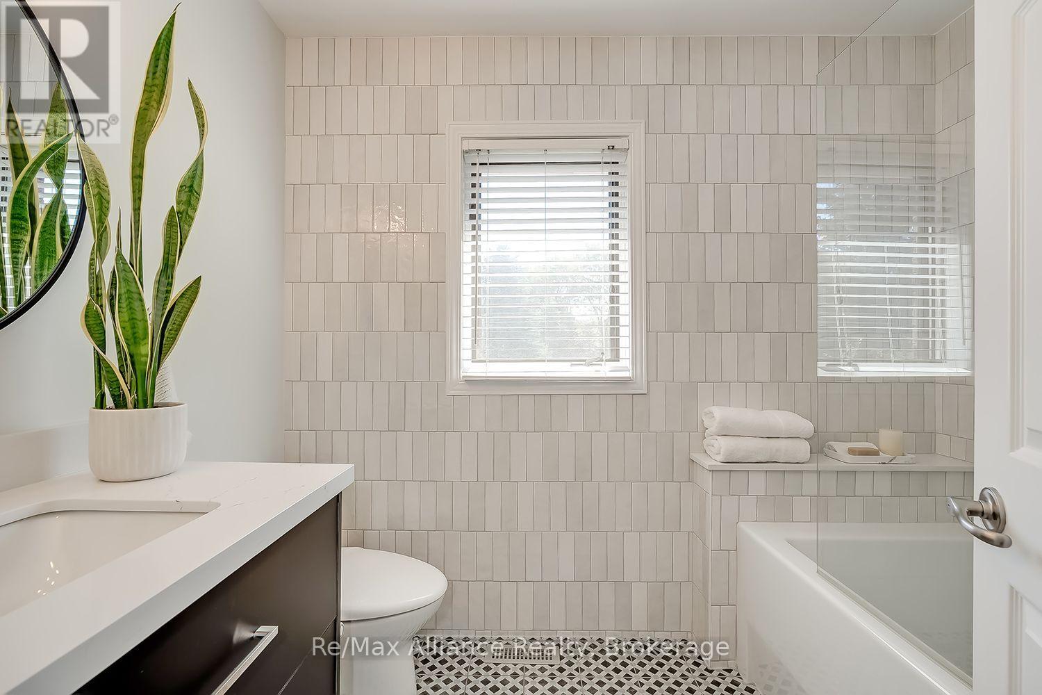 Bathroom with white vertical tile, glass-screened tub, dark vanity, and patterned floor.