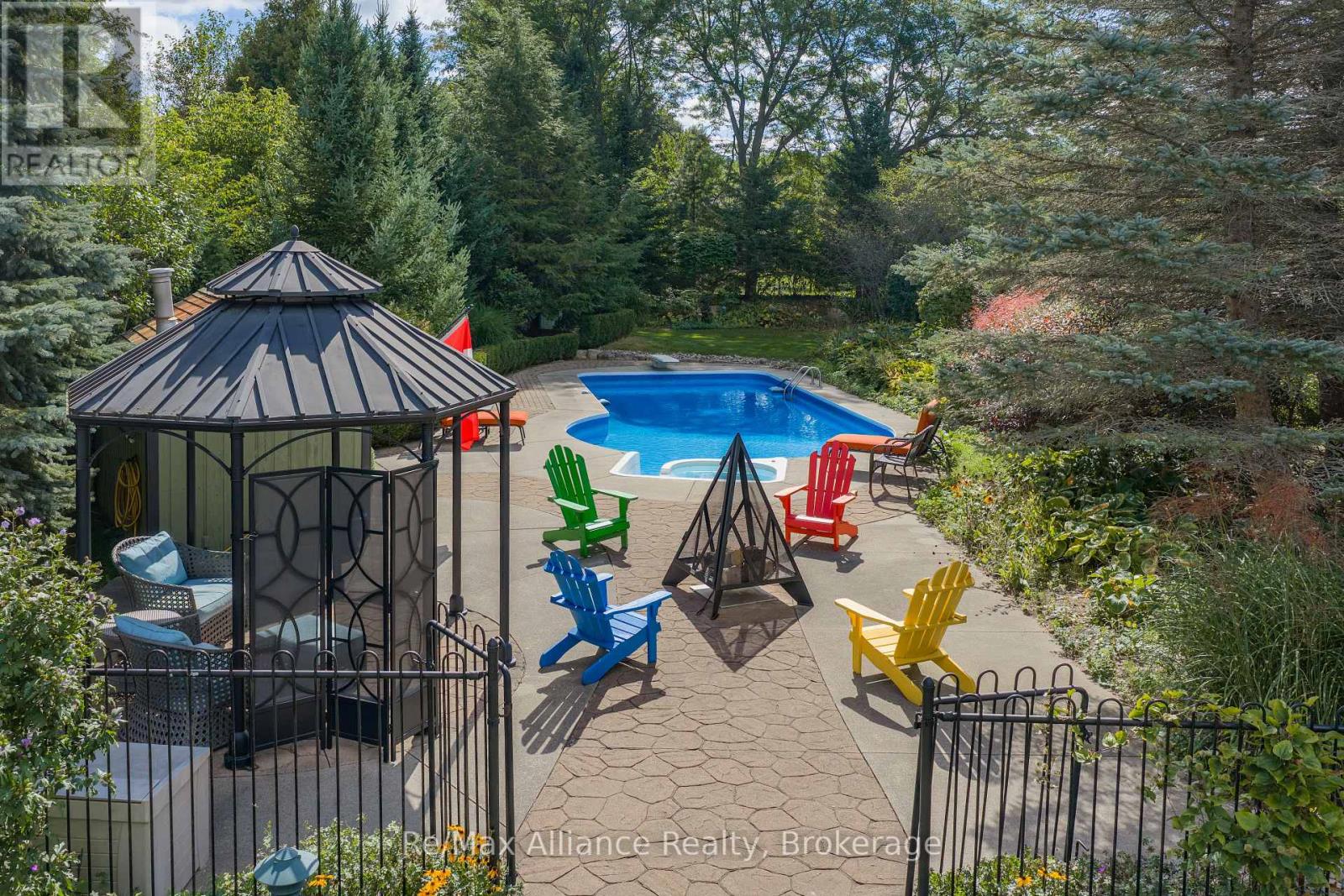 Backyard pool and stone patio with a gazebo, colorful chairs, and a fire pit.