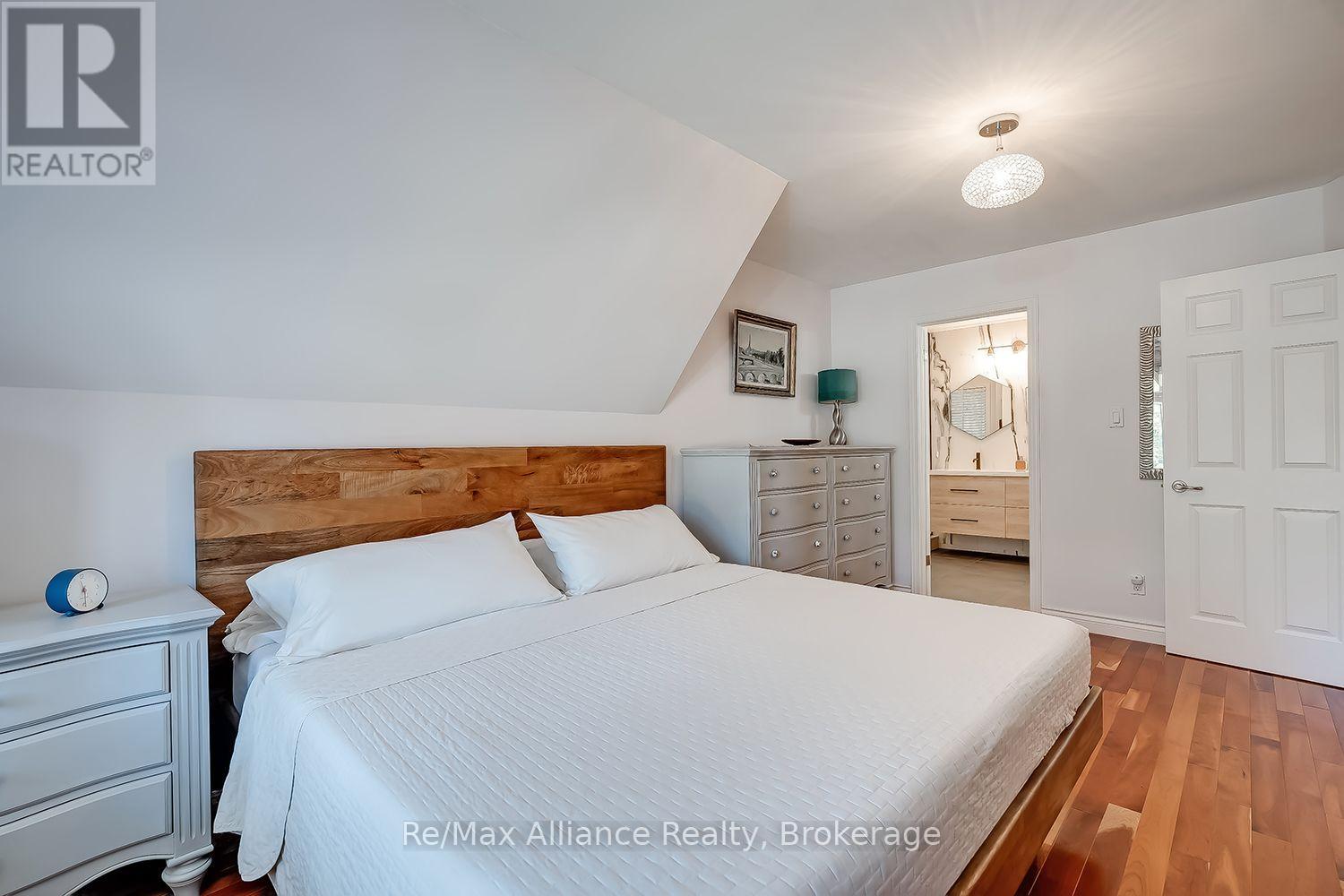 Bedroom with a white bed, wood headboard, hardwood floors, and an ensuite bathroom doorway.