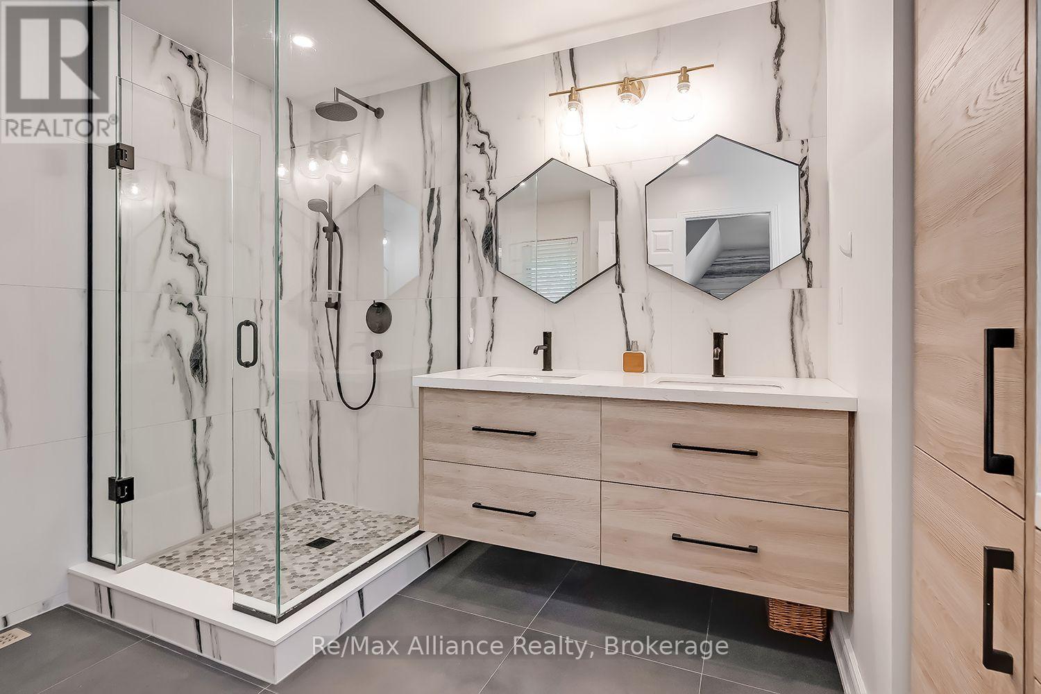 Modern bathroom with a glass walk-in shower and light wood double vanity beneath two angular mirrors.