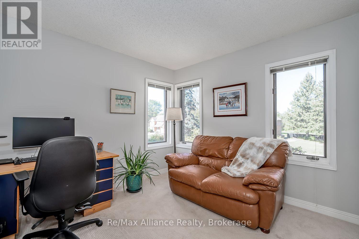 Furnished home office with a computer desk, black chair, brown leather sofa, and three bright windows.