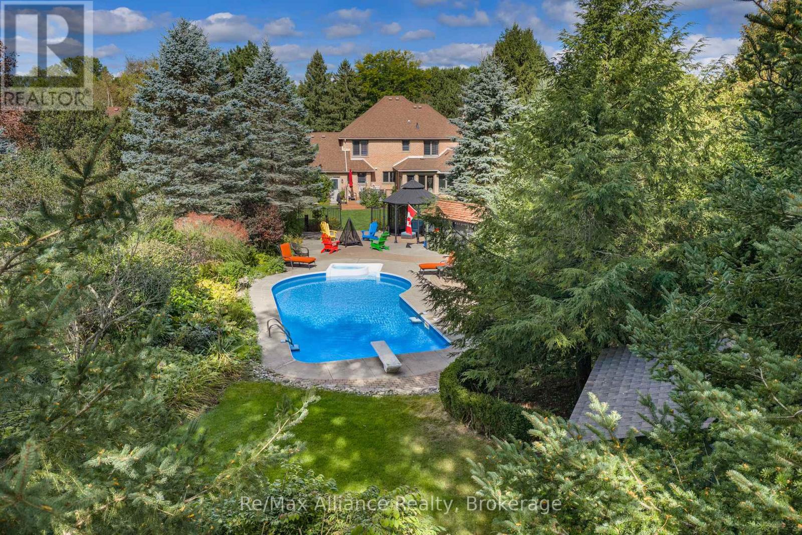 Aerial backyard view with a swimming pool, colorful patio chairs, mature trees, and a brick house.