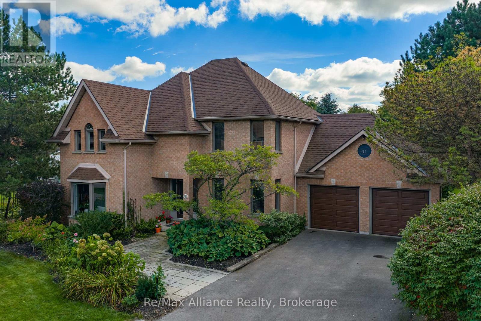 Two-story brick house with a brown shingle roof, landscaped front garden, and two-car garage.