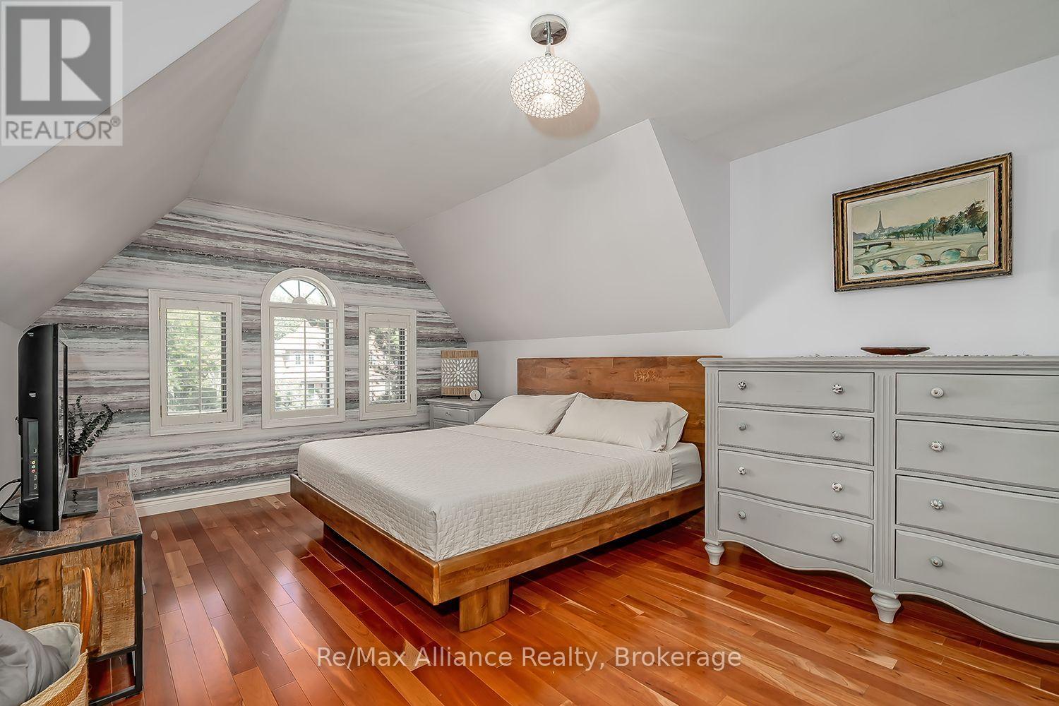 Furnished bedroom with a wooden bed, sloped ceiling, arched window, and weathered-board accent wall.