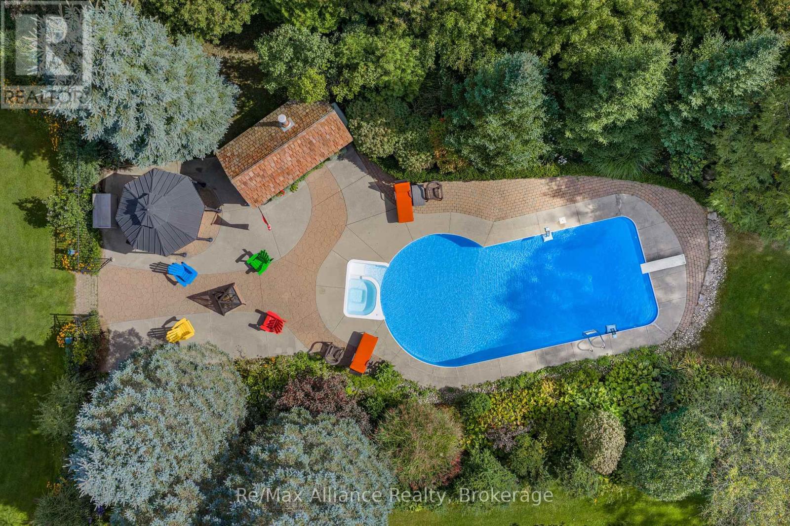 Aerial view of a swimming pool and landscaped patio surrounded by mature trees.