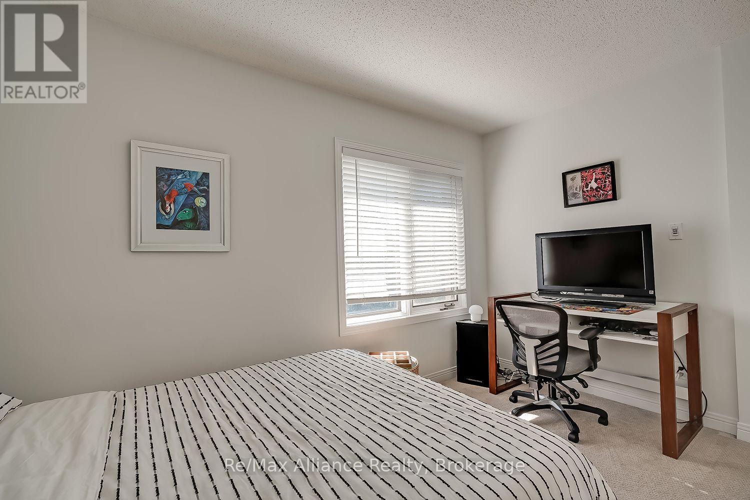 Bedroom with a striped duvet, a desk and television, and a window with blinds.
