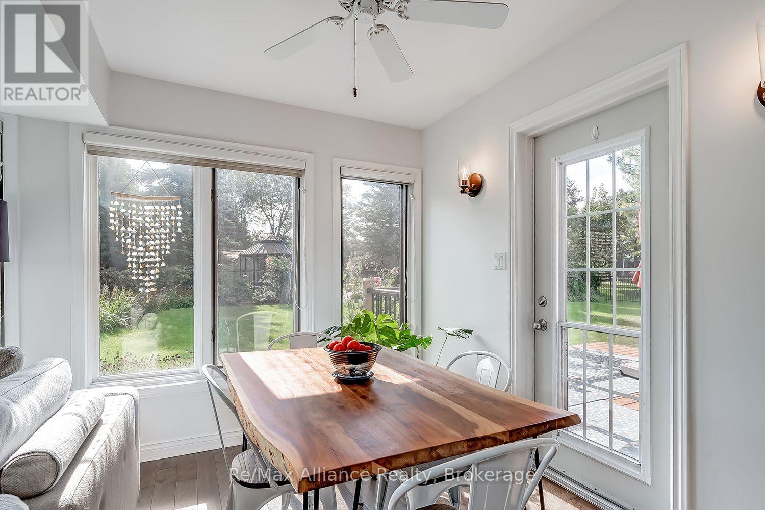 Dining area with a long wooden table beside large windows overlooking a green backyard.