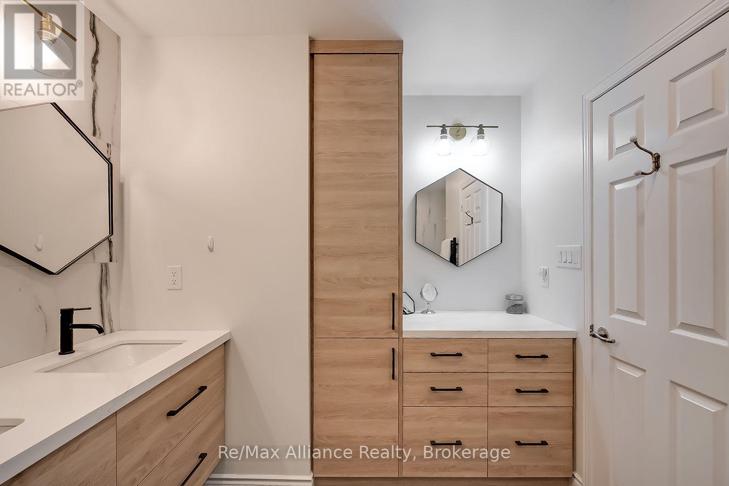 Bathroom with light wood vanities, a tall central cabinet, geometric mirrors, and black fixtures.