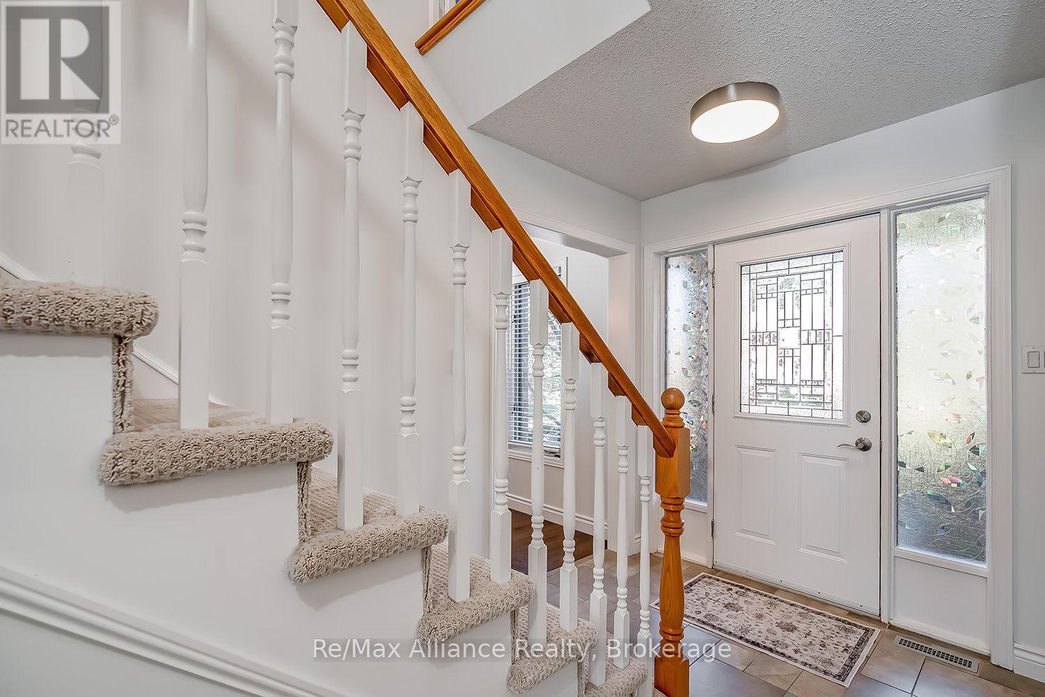 Front foyer with a carpeted staircase, wooden handrail, and front door with decorative glass sidelights.
