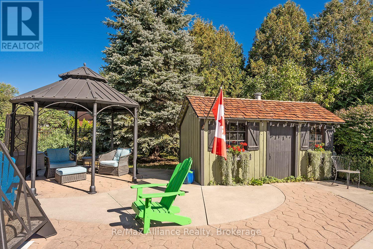 Backyard patio with a gazebo, cushioned seating, garden shed, Canadian flag, and bright green Adirondack chairs.