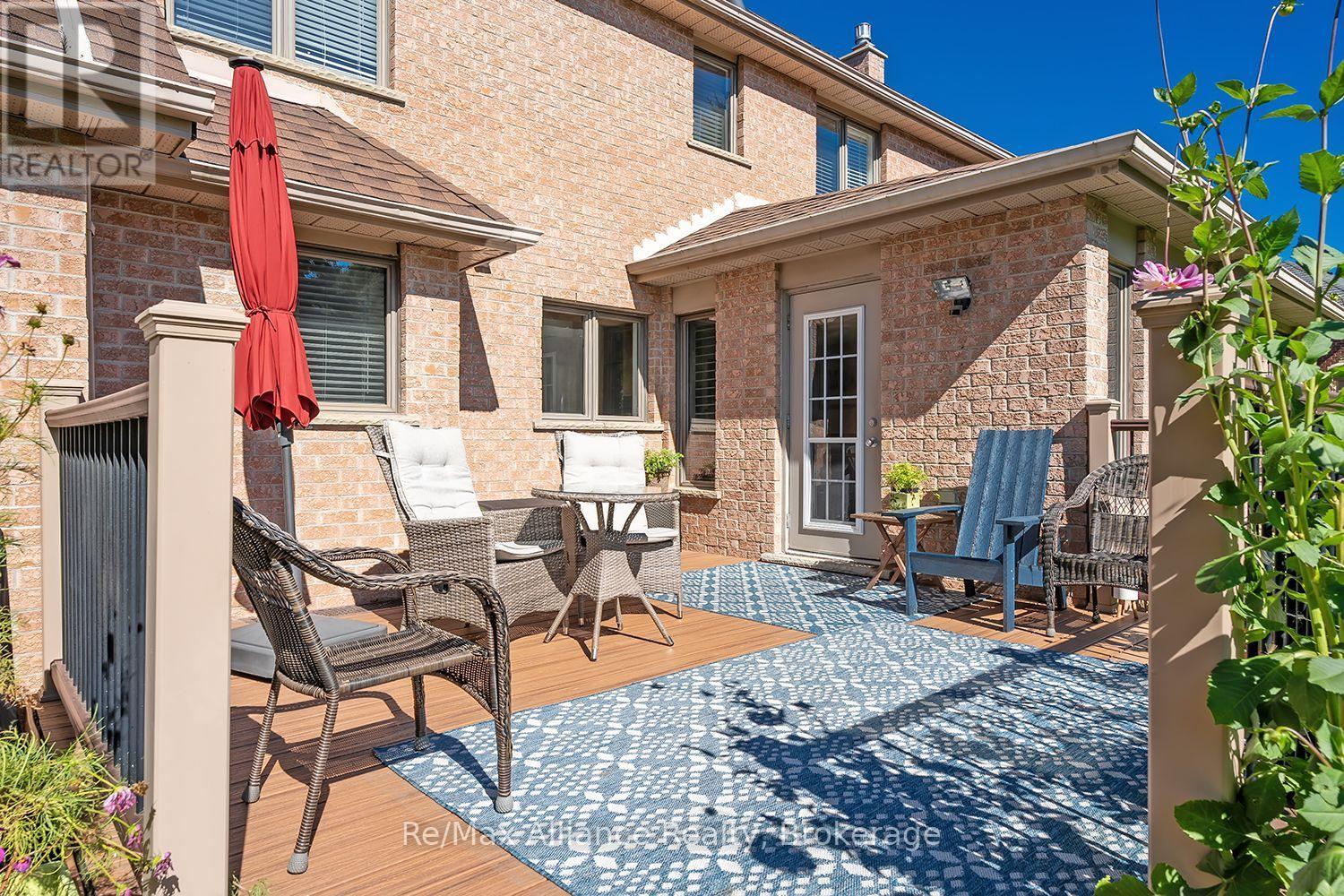 Brick home’s furnished backyard patio with wicker seating, a blue chair, and a red umbrella.