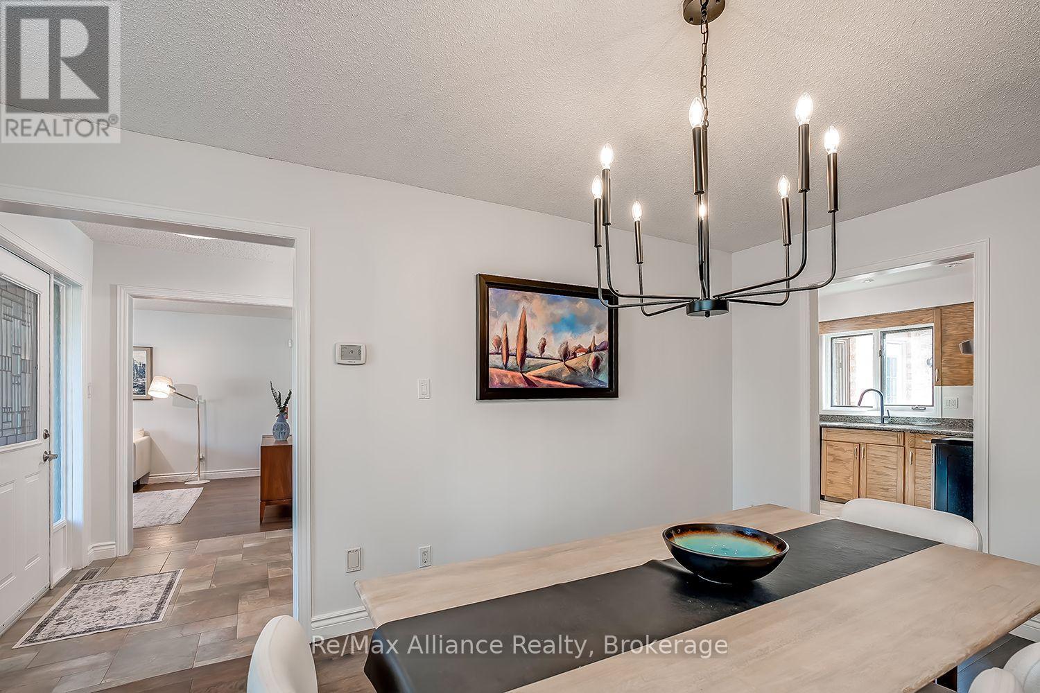 Dining room with a light-wood table and modern chandelier, opening to the kitchen and entry hall.