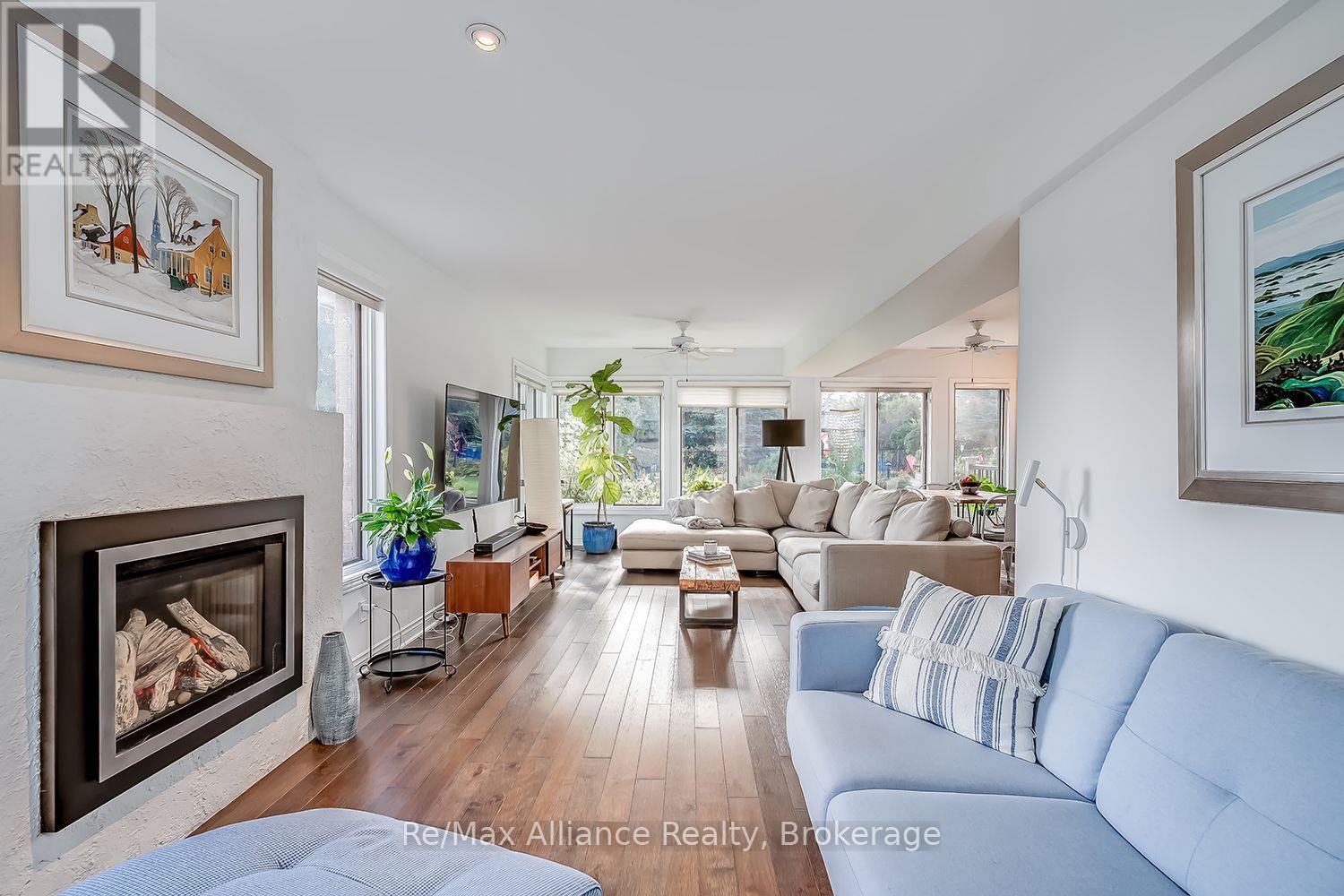 Bright living room with a fireplace, hardwood floors, and large garden-facing windows.