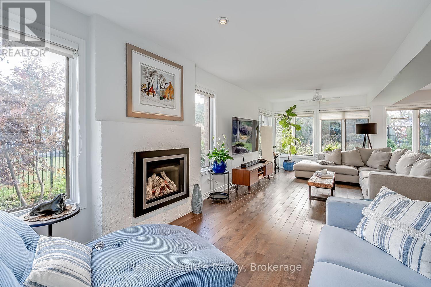 Living room with a white fireplace, wood floors, and large garden-facing windows.