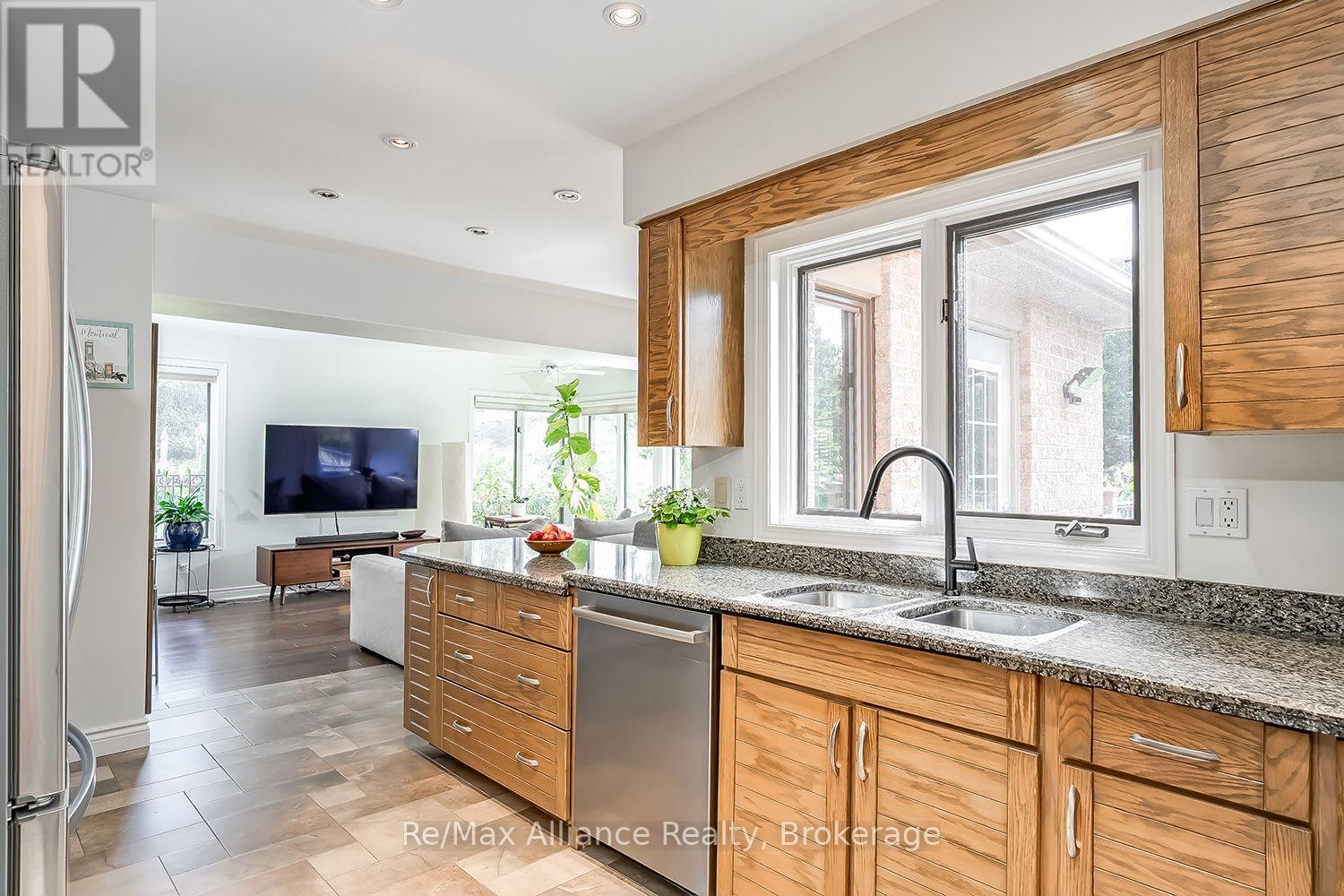 Kitchen with warm wood cabinets, granite counters, stainless-steel dishwasher, and a large window over the sink.