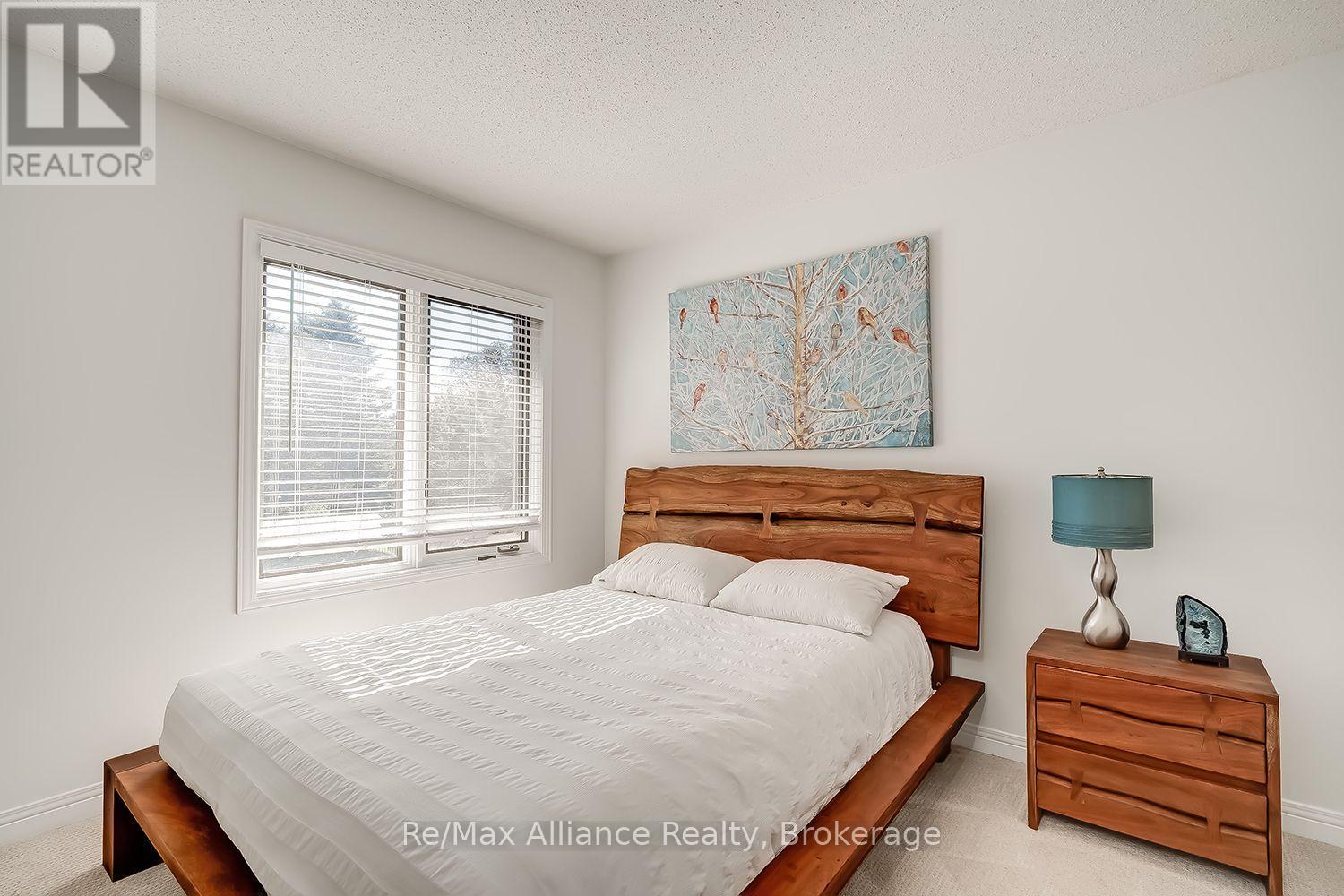 Bedroom with a wooden bed frame, bright window with blinds, and matching wooden nightstand.