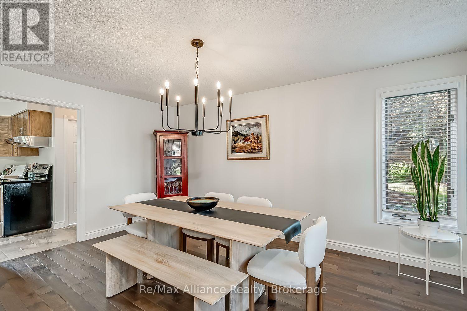 Dining room with a pale wood table and bench, chandelier, red glass-front cabinet, and tall plant by the window.