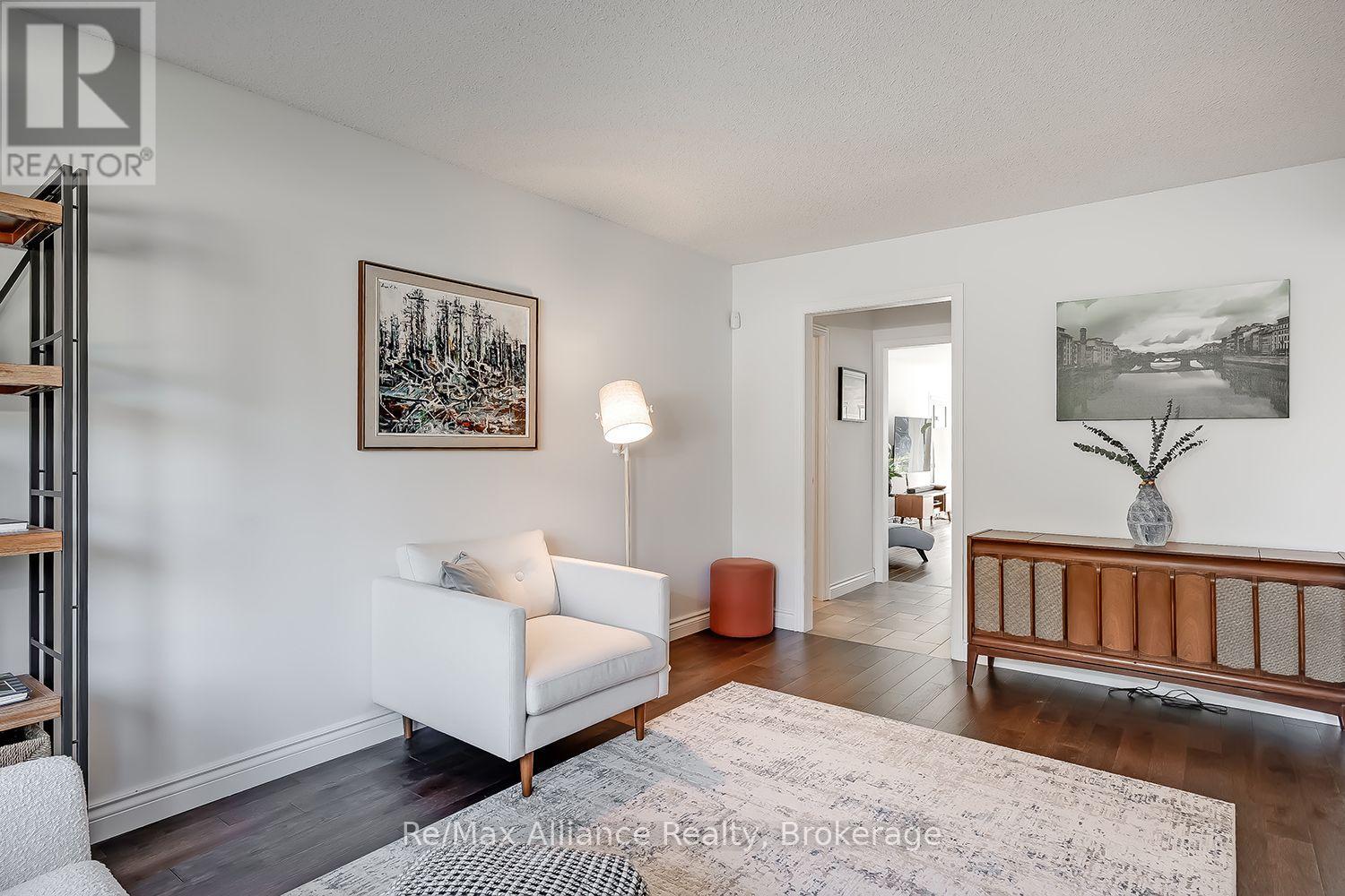 Furnished living room with a white armchair, pale rug, and mid-century wooden sideboard.