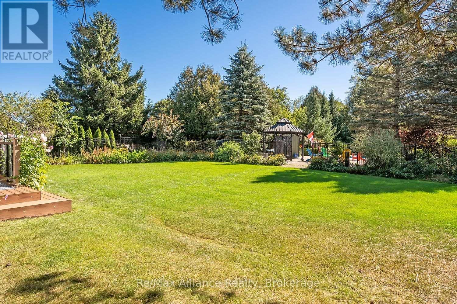 Backyard with a broad green lawn, mature trees, fenced garden beds, and a gazebo.