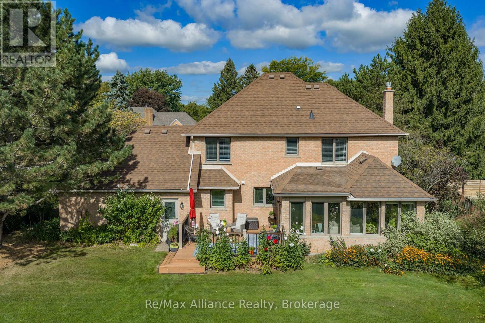 Rear of a brick house with a large shingle roof, deck, covered sunroom, and landscaped lawn.