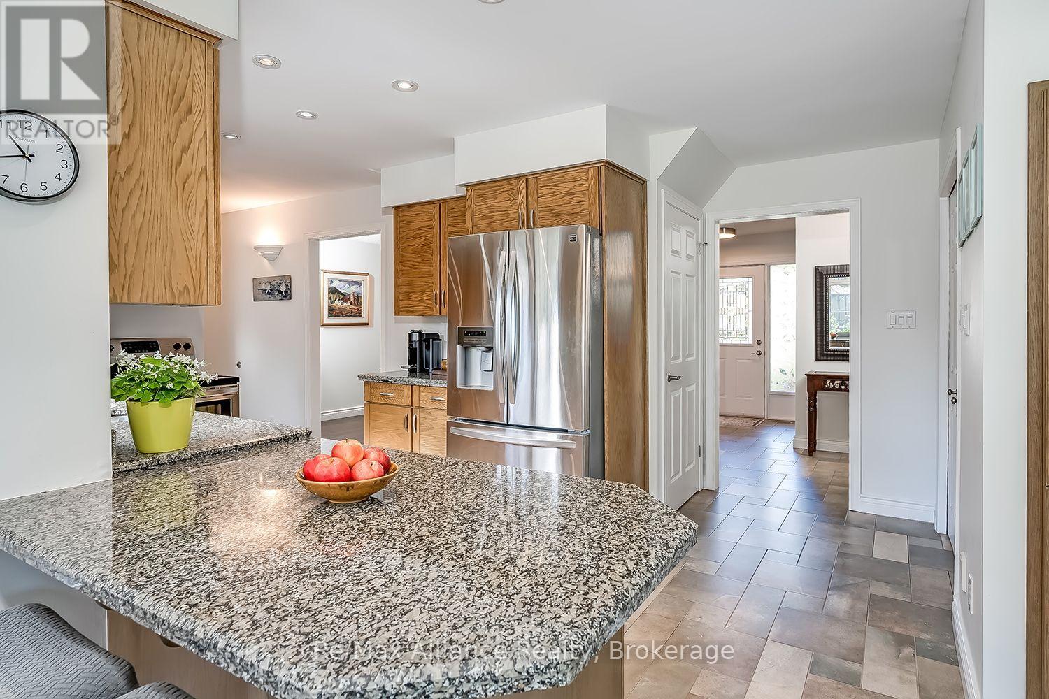 Kitchen with oak cabinets, stainless steel refrigerator, and a large granite island topped with fruit.