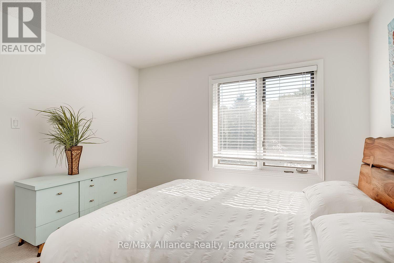 Furnished bedroom with a white bed, wooden headboard, pale green dresser, and window with blinds.