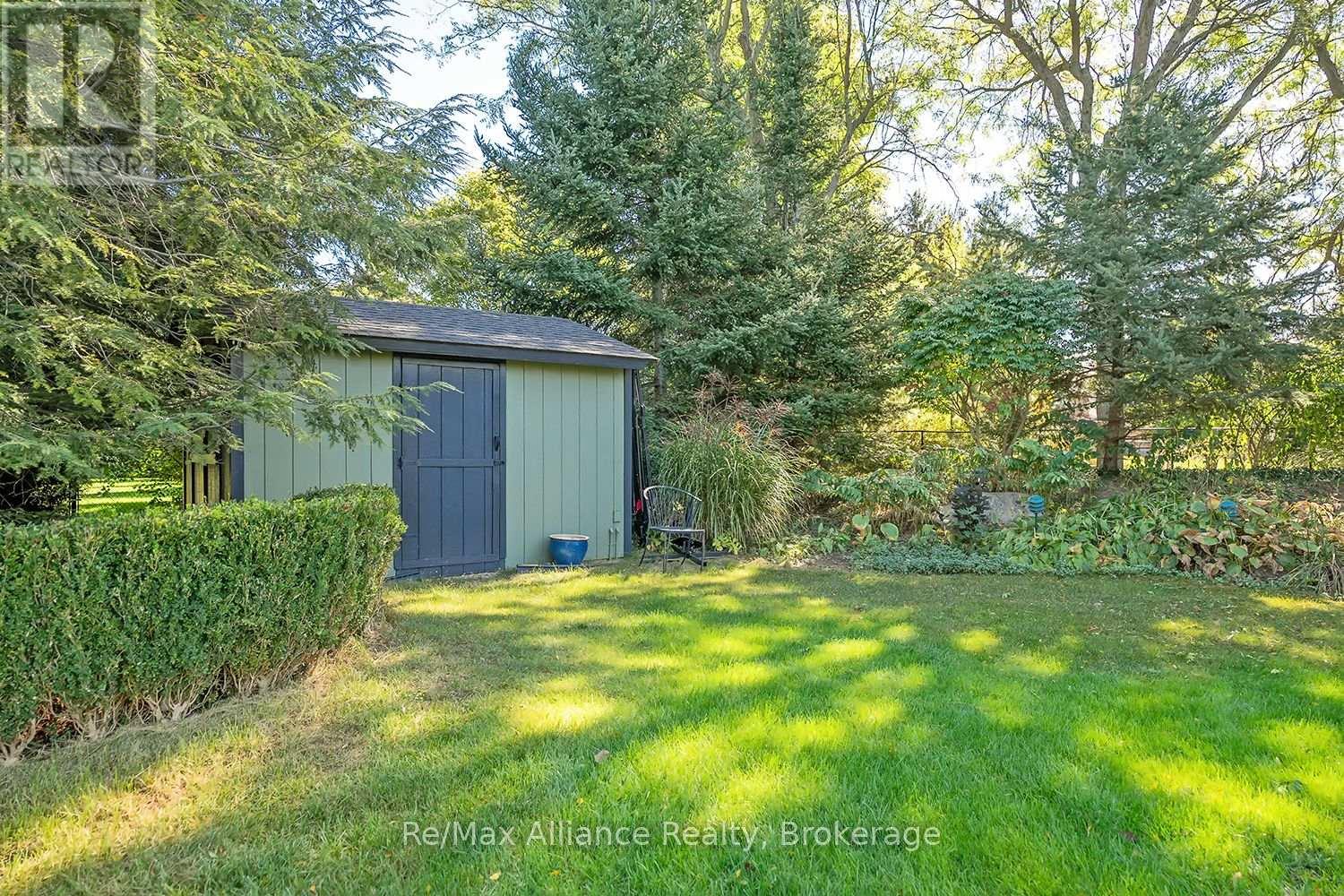 Backyard with a green garden shed, dark blue door, trimmed hedges, and mature trees.