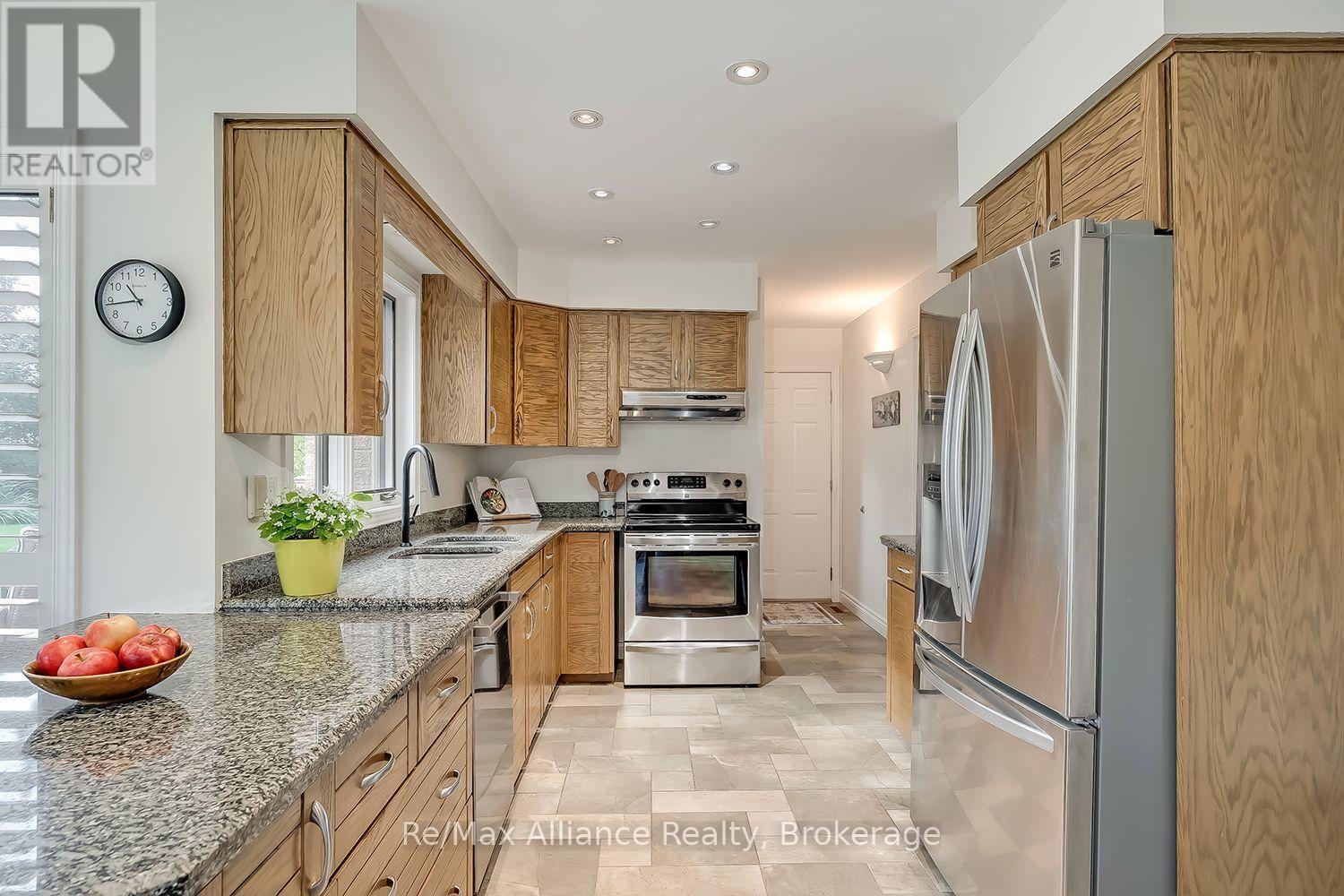 Galley kitchen with wood cabinets, granite counters, stainless-steel appliances, and a bowl of apples.