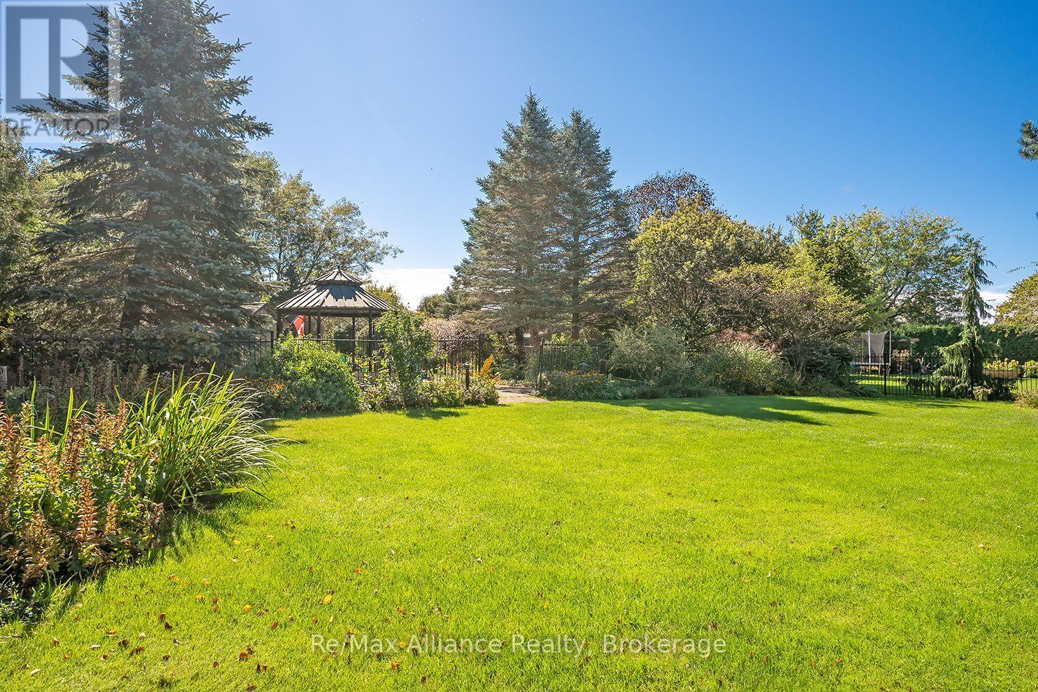 Landscaped backyard with a wide lawn, mature trees, garden beds, and a gazebo.