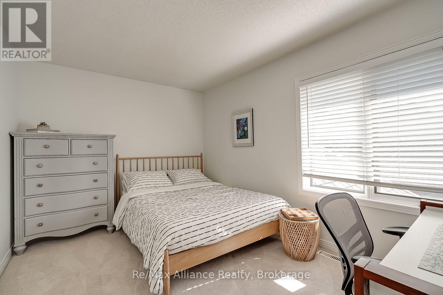 Furnished bedroom with striped bedding, a wooden bed, and a large window with white blinds.