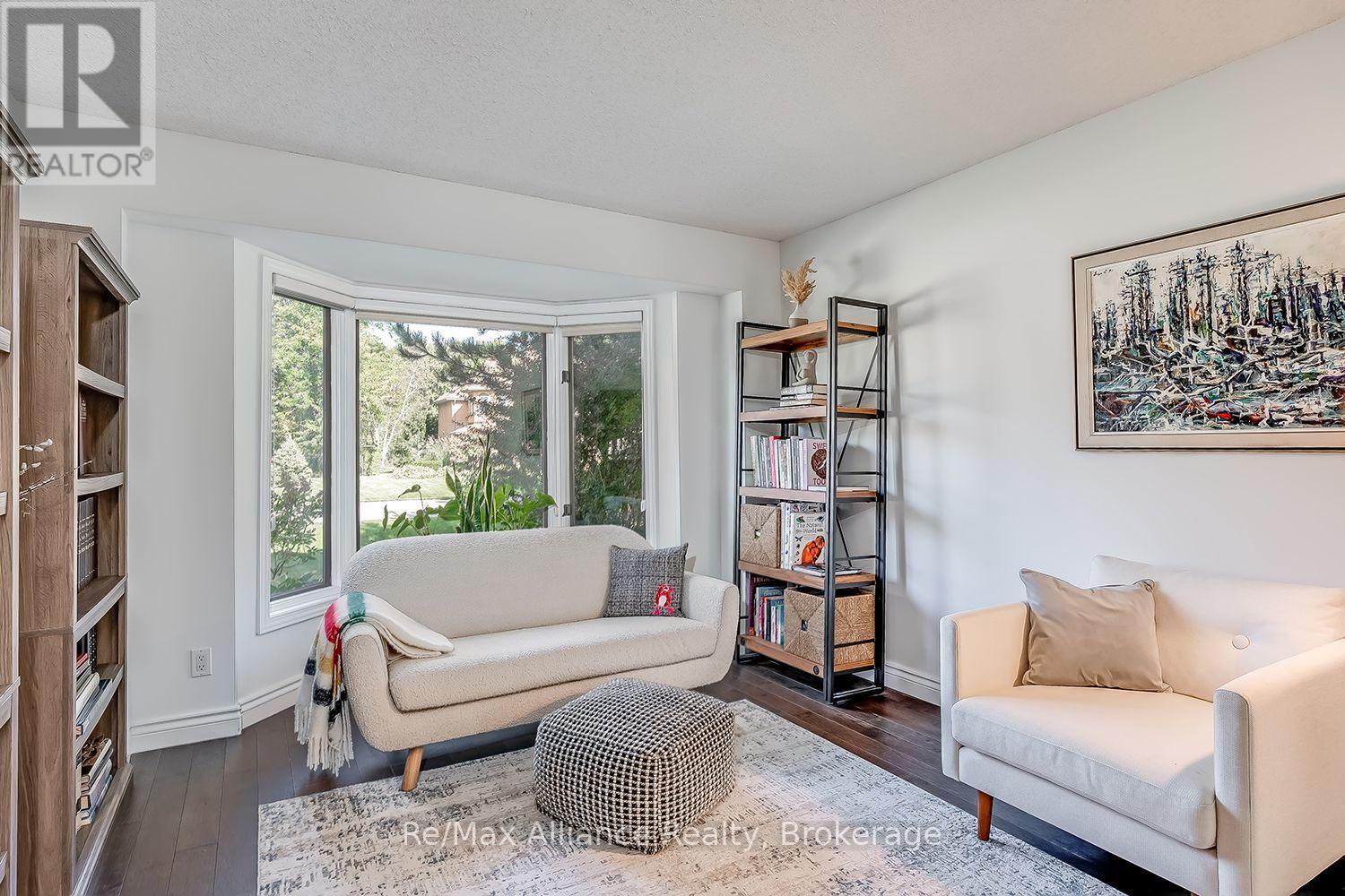 Living room with cream sofas, a patterned ottoman, and a large bay window overlooking greenery.