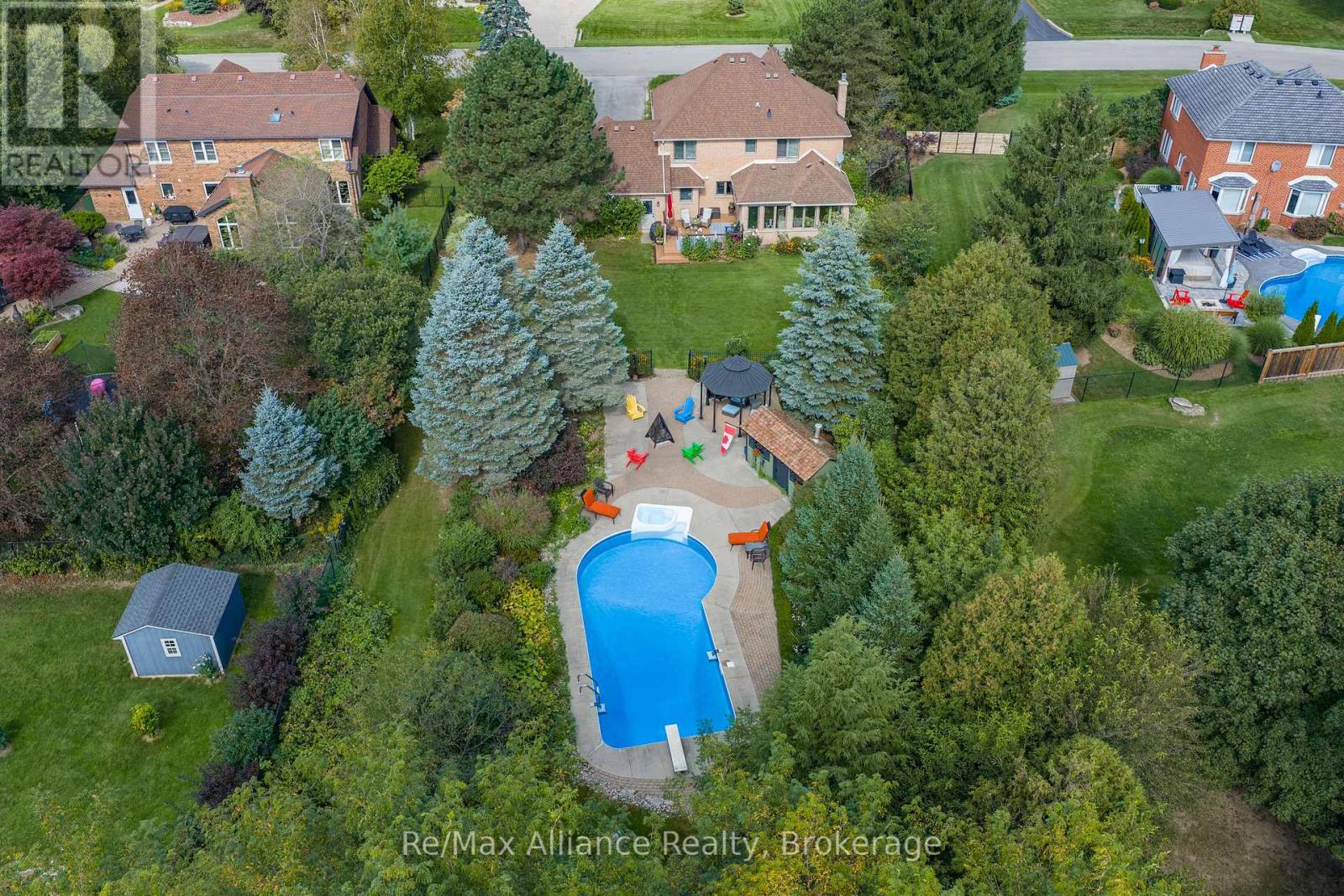Aerial view of a brick home with a long backyard pool, landscaped patio, and gazebo.